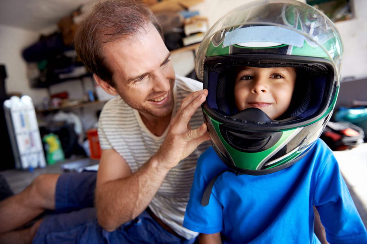 portrait of young boy playing with fathers motorbike helmet and helping his dad with fixing a motorcycle in the garage